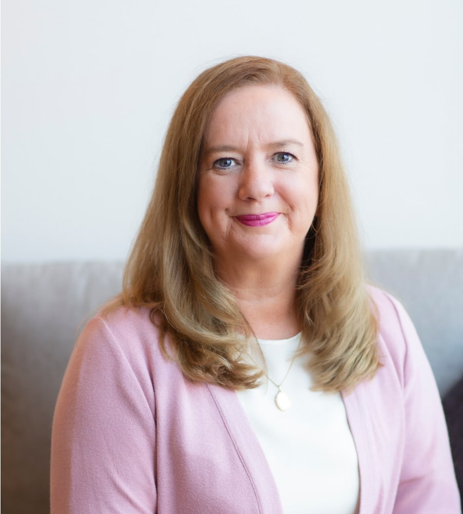 Annette Kuschert smiling at the camera wearing a pink cardigan and with top.