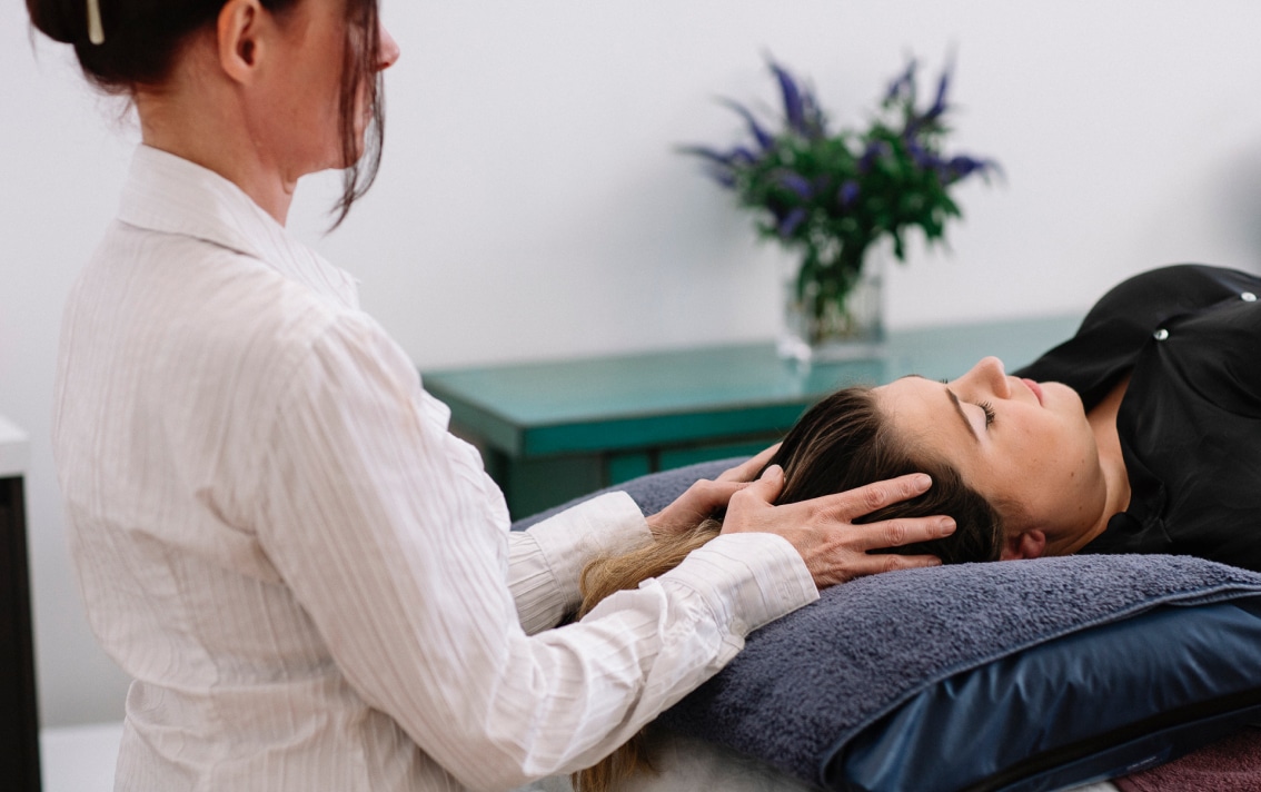 A practitioner gently touches a patients head while they lay down.