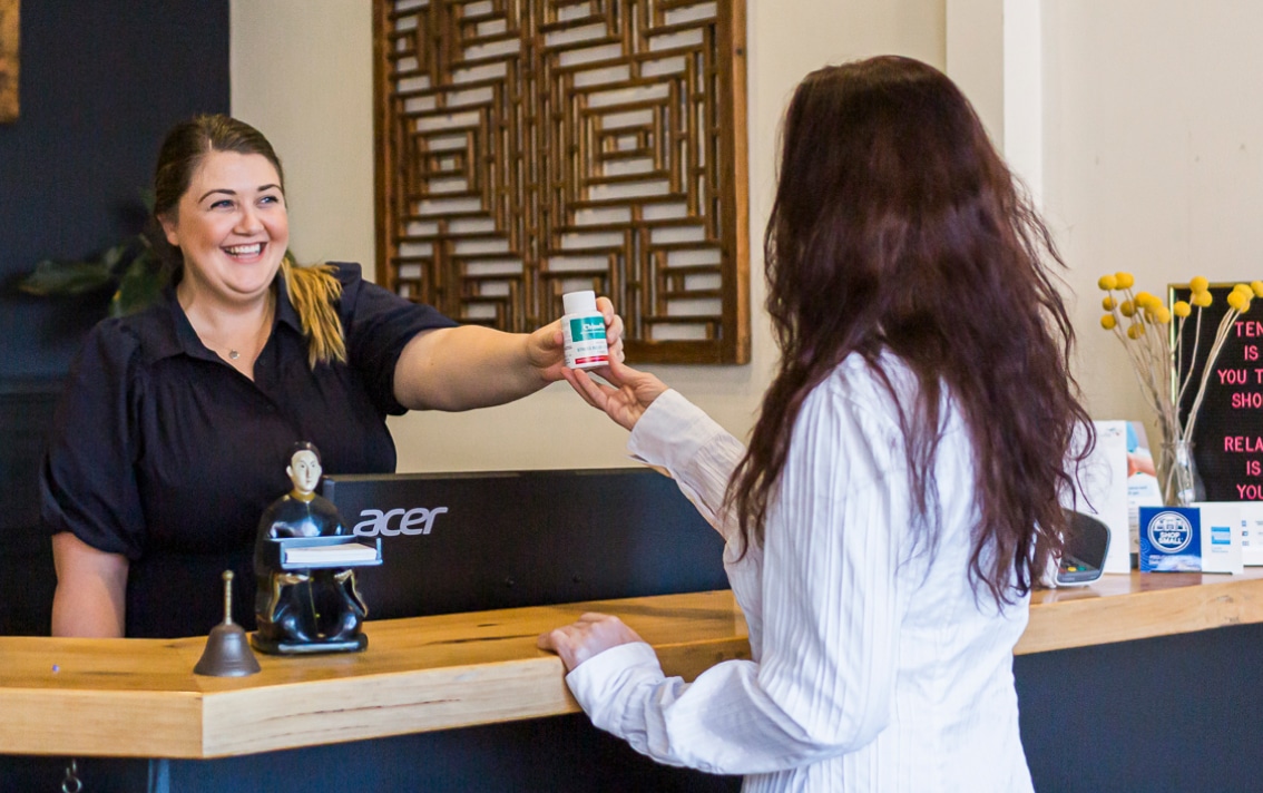 A practitioner smiles as she hands a bottle of Chinese medicine to a patient.